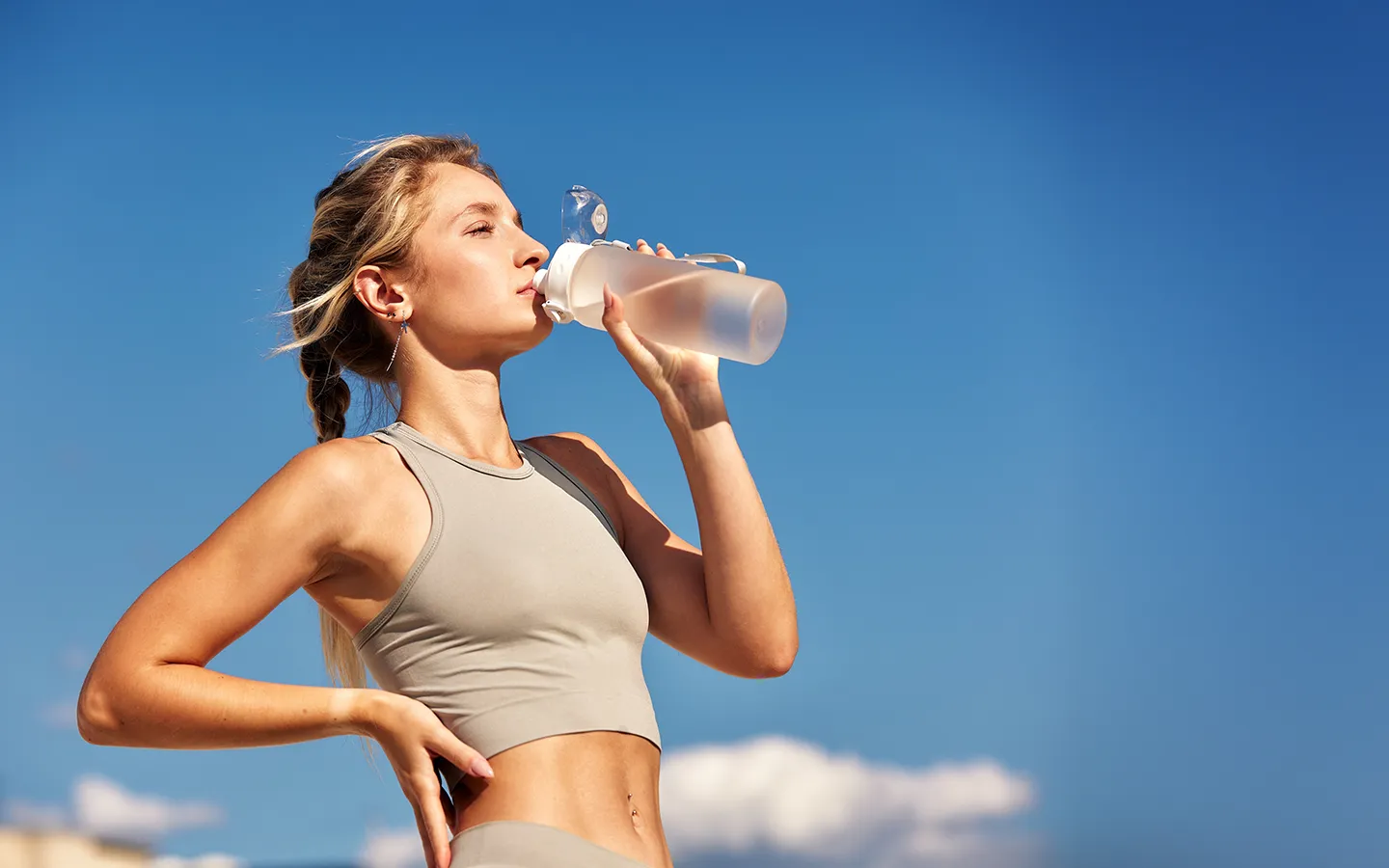 Sportliche Frau trinkt Wasser vor blauem Himmel – aktiv und gesund leben